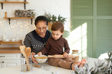 Granny and boy playing and having fun at Christmas decorated kitchen. Happy family waiting for the holidays.