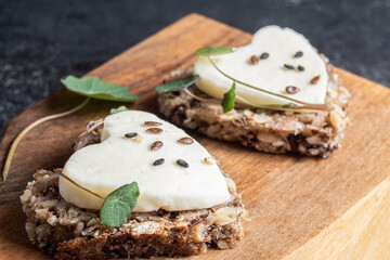 Heart shaped mini canapes with goat cheese and edible nasturtium leaves on a wooden board. View from above.