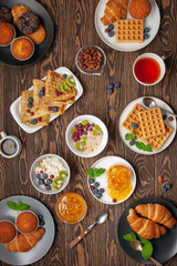 Continental breakfast. Top view. Flat lay. Coffee, tea, croissants, jam, egg, pancakes, maffins and oatmeal. Wooden background. Family breakfast table.