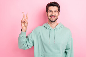 Fototapeta premium Photo of young positive toothy beaming smiling guy wear khaki hoodie showing v-sign hello friendly greetings cadre isolated on pink color background