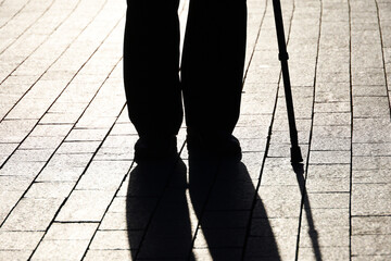 Silhouette of limping man walking with a cane, black shadow on pavement. Concept for disability, old age, blind person, dramatic life - obrazy, fototapety, plakaty
