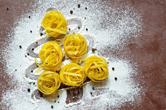 Raw yellow italian pasta (nests) pappardelle, fettuccine or tagliatelle in the shape of a Christmas tree on a brown background, close up. Egg homemade noodles cooking process,festive mood.