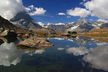 Panoramic view of the landscape with a smooth surface of the lake Riffelsee, mountains and clouds reflected in it, on a mountain Gornergrat, near Zermatt, in southern Switzerland