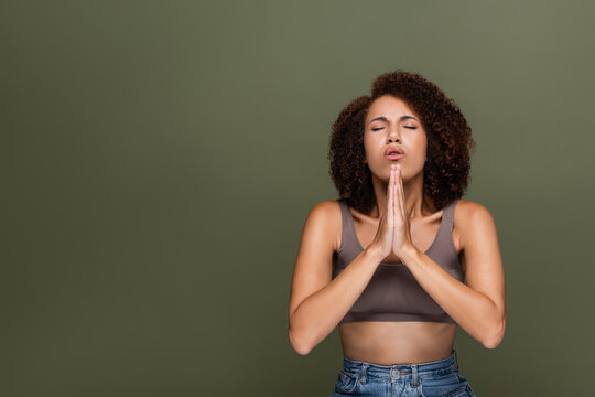 Curly african american woman with closed eyes praying isolated on green.