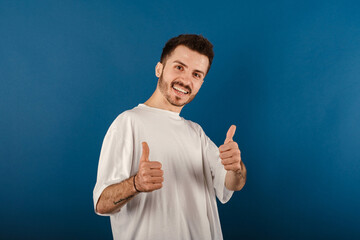 Cheerful caucasian man wearing casual clothes posing isolated over blue background smiling and showing thumbs up at camera. Approving expression looking at the camera showing success.