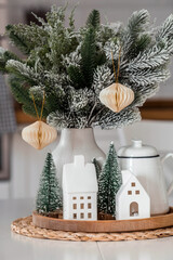A spruce bouquet and Scandinavian houses on a white kitchen table. Christmas decorations in the interior. The concept of preparing for the New Year holiday.