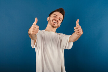 Happy casual man wearing t-shirt posing isolated over blue background doing hand gesture for great...