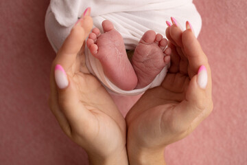 The palms of the father, the mother are holding the foot of the newborn baby in a pink blanket. Feet of the newborn on the palms of the parents. Photography of a child's toes, heels and feet.