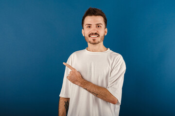 Portrait of young handsome man wearing white t-shirt posing isolated over blue background pointing...