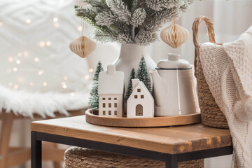 A bouquet of fir trees, a plaid in a wicker basket and Scandinavian white houses on a wooden table...