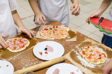 Cooking lessons for kids. On corner of wooden kitchen table are three shaped pizza pieces, ready to be baked. Children's figures stand nearby and finish product.