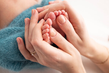 Mother is doing massage on her baby foot. Close up baby feet in mother hands on a blue background. Prevention of flat feet, development, muscle tone, dysplasia. Family, love, care, and health concept