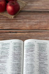Red apples and open Holy Bible Book on wooden background with copy space. Vertical shot. Top view.