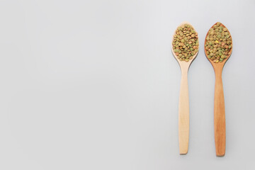 small grains of natural green lentils in a wooden spoon on a gray background