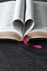Open Holy Bible Book with golden pages folded in a heart shape on dark background with copy space. Vertical shot. Christian biblical concept of love and faith.