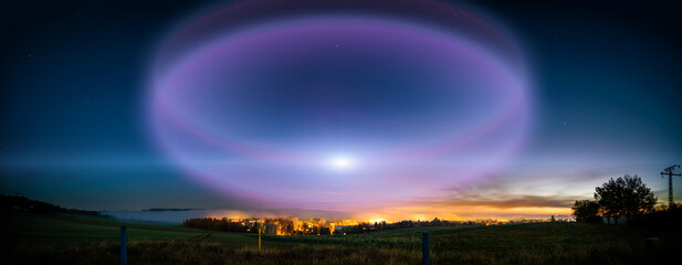 lunar halo in the night sky and city light on the horizon