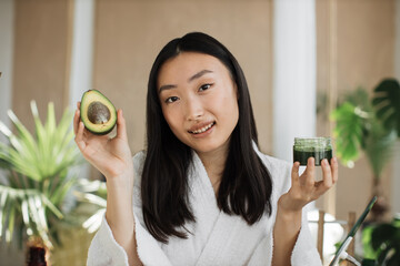 Blogger or content creator asian woman preparing natural cosmetics at home holding avocado homemade...