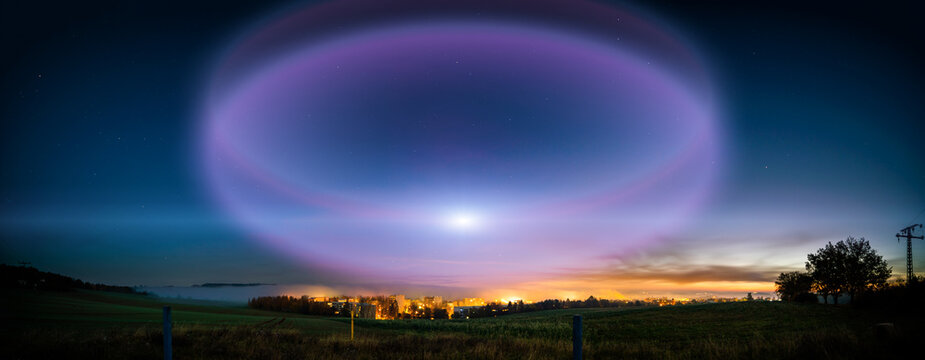 lunar halo in the night sky and city light on the horizon