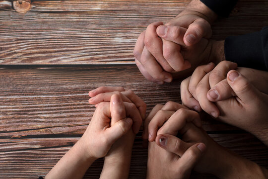 Praying hands on a wooden background with copy space. Top table view. Young Christian friends and family pray together to God Jesus Christ in faith. Biblical concept of prayer, support, and praise.