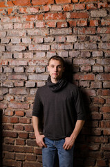 young man in a black jacket against the background of a brown, red and black brick wall