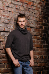 Obraz premium young man in a black jacket against the background of a brown, red and black brick wall