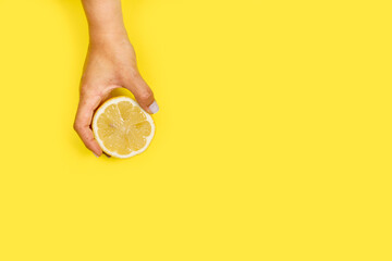 Mano de mujer sosteniendo una rodaja de limón  sobre un fondo amarillo liso y aislado. Vista superior y de cerca. Copy space