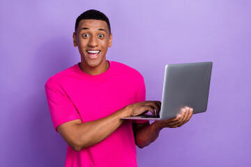 Portrait of impressed ecstatic man fade haircut wear pink t-shirt open mouth hold laptop write email isolated on violet color background