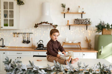 Portrait of toddler boy playing and having fun at Christmas decorated kitchen. Happy kid waiting for the holidays.