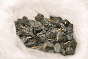 Blue raisins with sprigs in a transparent bag on a white table with partially blurred focus.