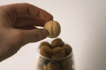 A man holds a walnut in his hand over a glass vase with nuts.