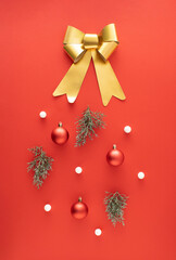 Golden bow, red Christmas baubles, evergreen branches and white balls on red background. Minimal New Year concept.