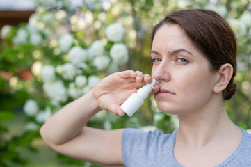 Caucasian woman uses a nasal spray while walking in the park.