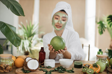 Focus on hands of beautiful young asian woman with green cosmetic mask on face and towel on head...