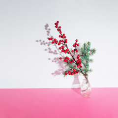 Minimal winter holidays composition with one decorative branch of Christmas tree and red berries in a transparent bottle. Xmas and New Year concept.