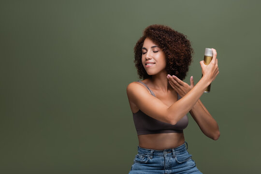 Smiling african american woman applying hairspray isolated on green.