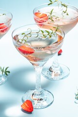 Glasses with cold pink champagne or punch with wine strawberries, ice and rosemary on blue background