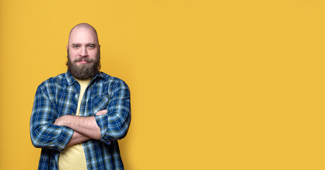 Obraz premium Bearded middle-aged caucasian man in casual blue clothes over yellow background. Male stands crossing arms on his chest looking at camera, Mock up, template, copy space. Positive advertising concept