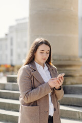 Fototapeta premium Beautiful smiling woman with smartphone walking on the street