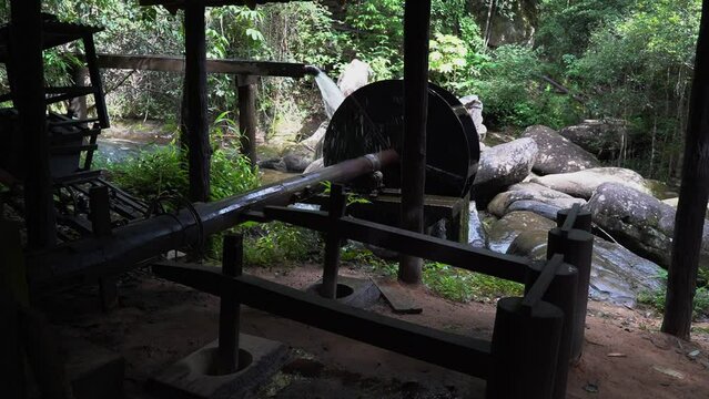 Wooden wheel of an old medieval water mill used for rice production 
 with background of a waterfall and forest.
