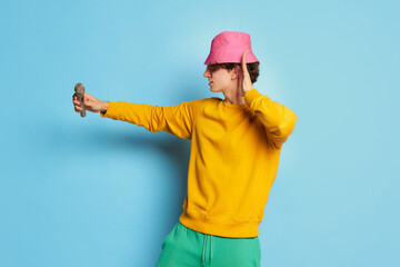 Portrait of young man with curly hair posing in pink panama and singing isolated over blue background. Performing
