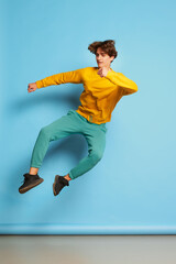 Fototapeta na wymiar Portrait of young man with curly hair posing in a jump isolated over blue background. Cheerful mood