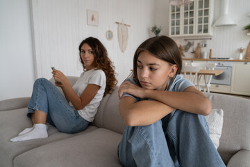 Obraz premium Unhappy teen girl feeling sad after argument with parent, offended teenager sitting separately with mother on sofa at home, upset child having misunderstandings with mom. Teen depression concept