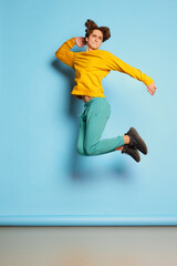 Obraz premium Portrait of young man with curly hair posing in casual bright clothes and jumping isolated over blue background