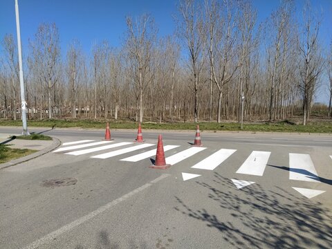 Painting pedestrian crossings with new paint. Road warning plastic orange cone. White stripes on the pavement. The pedestrian crossing is marked with special road signs or markings