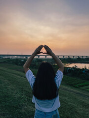 Girl making heart shape gesture under sunset