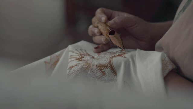 Close-up female hand holding canting for making of batik painting.