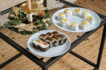 Sushi with salmon on a white plate, next to another plate with rolls. Christmas or New Year concept background.