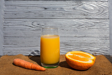 A composition of fresh vegetables, fruits, an orange and a carrot lying around an orange juice in a...
