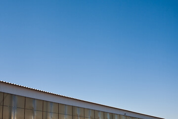 The upper part of an industrial building against the backdrop of a blue clear sky during the day. Background image for your design or illustrations.