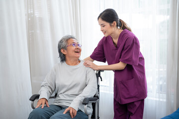 Asian young nurse taking care and talking mature female patient sitting on wheelchair in hospital. Healthcare concept.